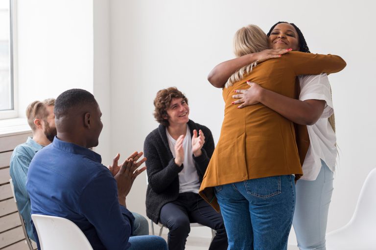 Candid shot of casually dressed professional woman psychotherapist in her fifties touching her young male patient by shoulder while having counseling session, expressing sympathy and support