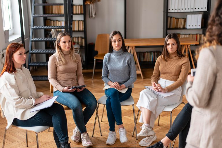 Candid shot of casually dressed professional woman psychotherapist in her fifties touching her young male patient by shoulder while having counseling session, expressing sympathy and support